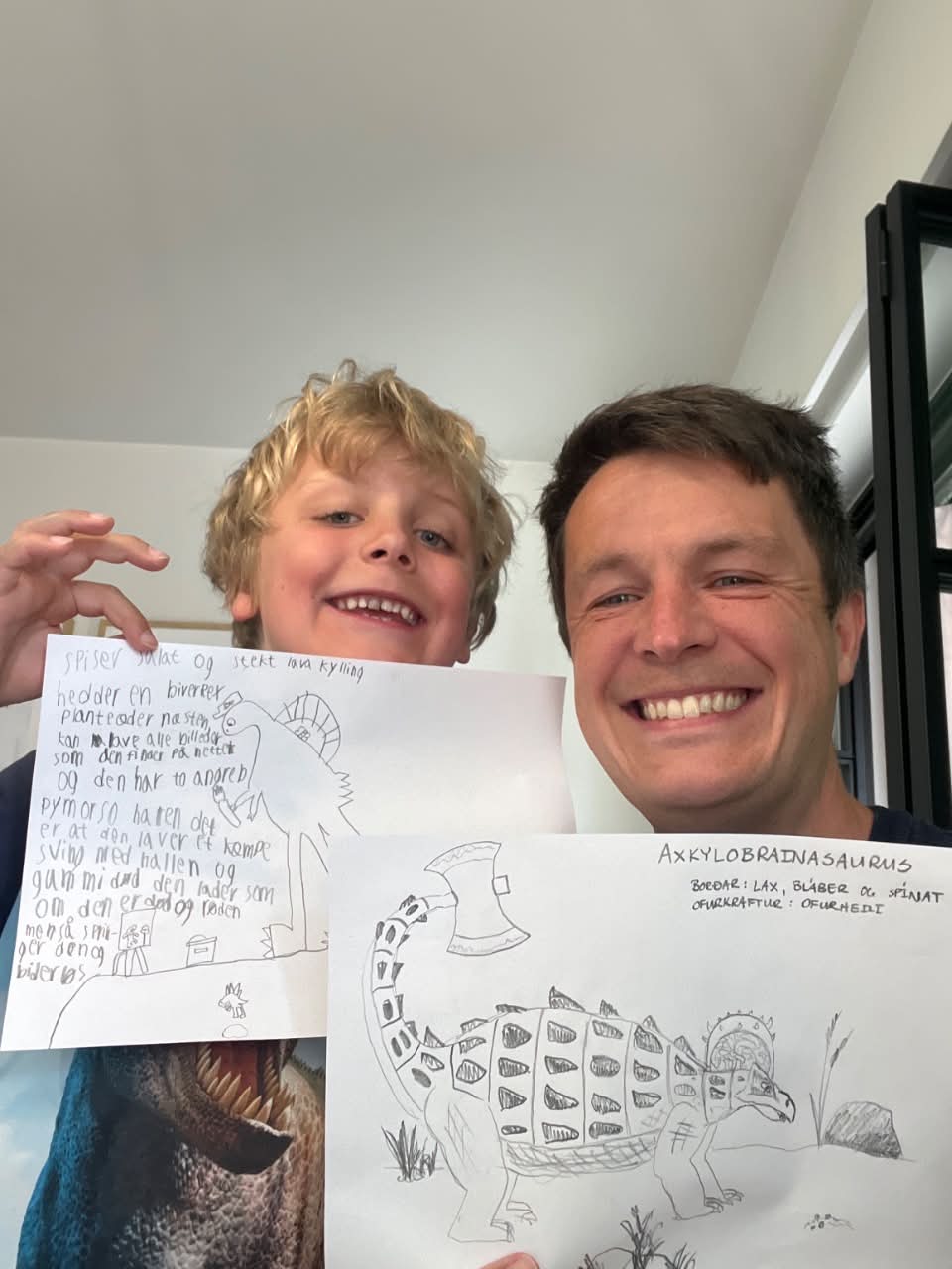 A father and his son holding up two hand-drawn dinosaurs they invented together